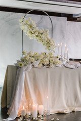 Wedding reception. Festive arch decorated composition flowers and candles in hall restaurant. Table newlyweds covered a tablecloth in banquet area on wedding party. Table setting. Celebration concept.