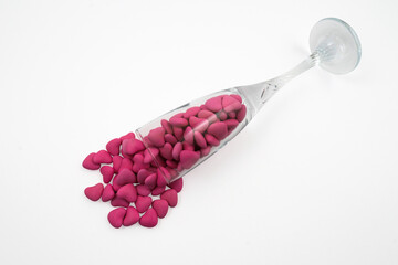 Overturned glass with heart shaped pink candies (close-up) isolated on white background