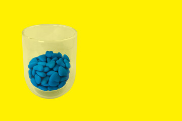 Glass with blue heart shaped candies (close-up) isolated on yellow background. State symbols of Ukraine