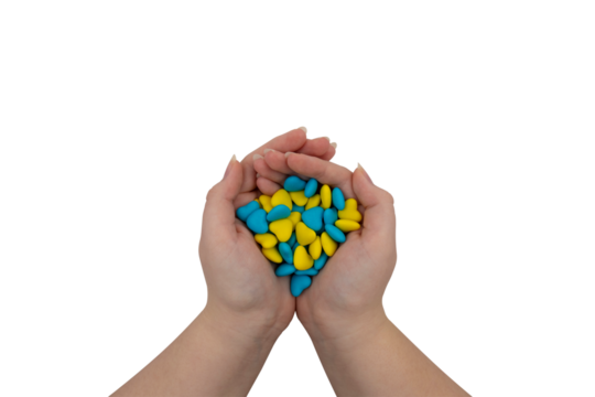 A handful of yellow and blue heart-shaped candies in hands on a transparent background. State symbols of Ukraine