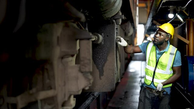 Engineer or maintenance worker repairing and inspecting train undercarriage in workshop.