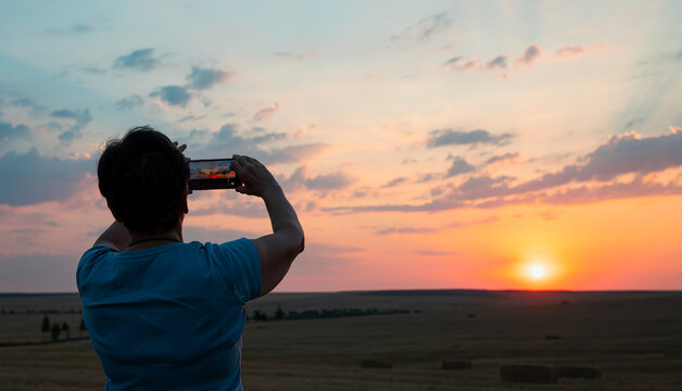 Woman holding mobile phone in hands and taking sunrise photo