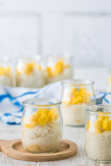 Coconut rice pudding with mango in dessert glasses on white wooden background, vertical