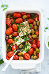 Baked feta cheese with cherry tomatoes and olives on a white table.