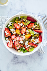 Fruit salad with feta and seeds in white bowl on white table. Healthy vegan detox summer recipe.