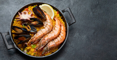 Traditional spanish seafood paella in the fry pan on a black background.