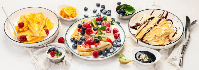 Sweet crepes assortment with berries chocolate on gray background. Homemade food concept. Top view, flat lay