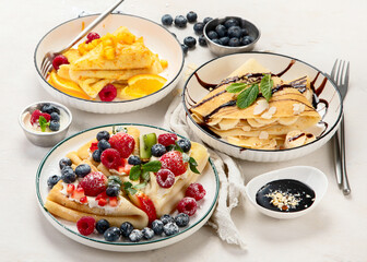Sweet crepes assortment with berries chocolate on gray background. Homemade food concept. Top view, flat lay