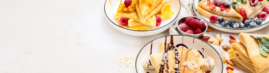 Sweet crepes assortment with berries chocolate on gray background. Homemade food concept. Top view, flat lay