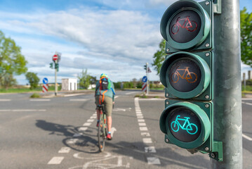 Ein unscharfer, nicht erkennbarer Radfahrer überquert auf dem Radweg eine Straßenkreuzung bei grüner Ampelphase