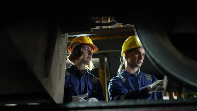 Engineer or maintenance worker repairing and inspecting train undercarriage in workshop.