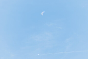 Fototapeta na wymiar The waning moon is in the daytime in the blue sky underneath a commercial airliner is flying