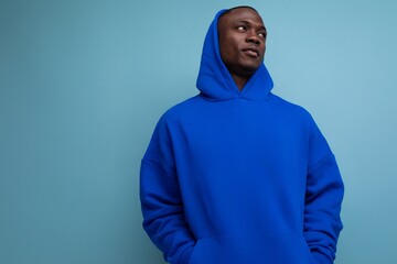 stylish cool young guy american with dark skin is dressed in a trendy sweatshirt with a hood on a studio background with copy space