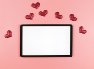 flat lay of digital tablet with blank white screen, red glitter hearts  isolated on pink background.