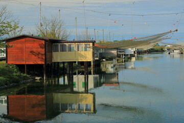 An old white and red fishing hut is reflected in the water of the Po Delta in Italy on a May afternoon.