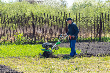 Farmer man plows the land with a cultivator preparing the soil for sowing
