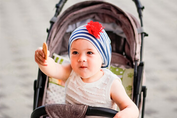 A happy child in a baby carriage. Funny girl in a scarf. The child eats cookies and hands them to others. A walk for children in the fresh air.