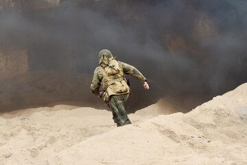 Historical reconstruction. An American infantry soldier from the World War II runs on the beach between smoke and dust.  View from the back.  Hel, Poland 