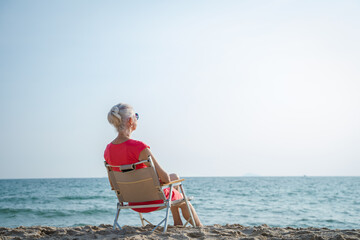 Happy retired woman relaxing on sand at the beach.