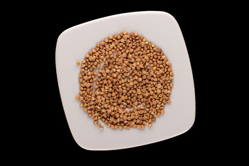 Raw buckwheat with white ceramic saucer isolated on black background, macro, top view.