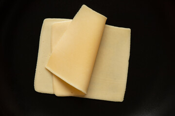 Slices of hard cheese lie on a black plate , food