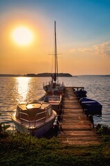 Fototapeta premium Sailing yacht and jetty in the beautiful lake. Empty wooden jetty with moored boats on the lake shore at the sunrise in Mazury region, Poland.
