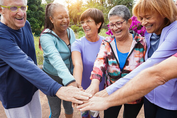 Happy senior people stacking hands together after yoga lesson outdoor at city park - Sport and...