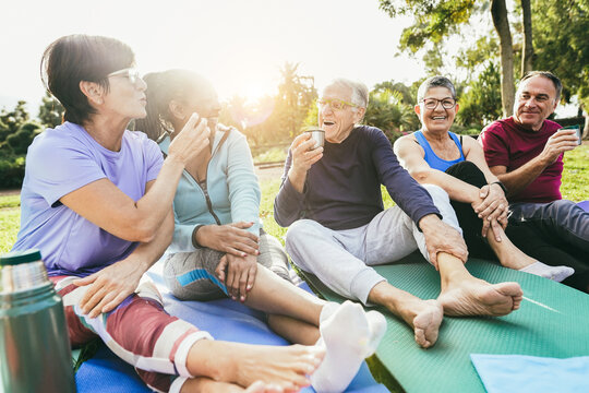Senior people having fun drinking hot tea after yoga lesson at city park - Multiracial mature friends laughing together - Joyful elderly lifestyle and sport concept - Main focus on center man face