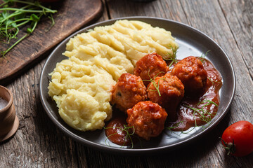 Mashed potatoes with meatballs in tomato sauce in a bowl