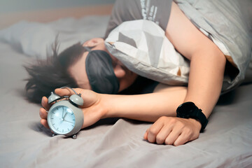 an is sleeping in his bed with an alarm clock in a hand.