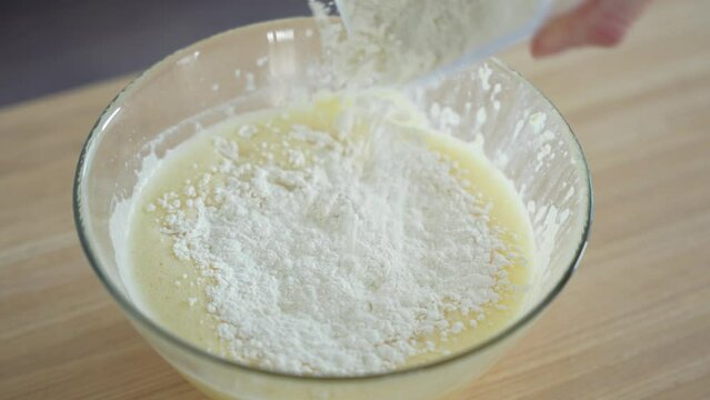 Close-up camera shot of dough preparation for waffles. Woman puts flour to the mixed eggs. Pancake culinary. Preparing breakfast in home kitchen.