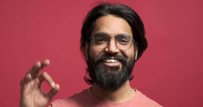 Closeup portrait of handsome young man with beard and eyeglasses smiling and showing ok hand sign against red background Generative AI