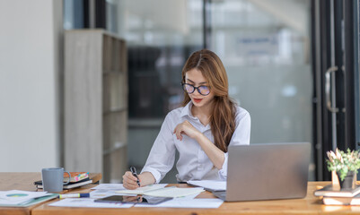 Asian Business woman using calculator and laptop at workplace doing math finance on an office desk, tax, report, accounting, statistics, and analytical research concept