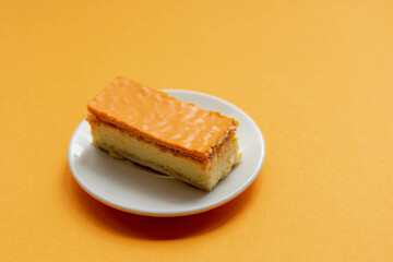 Celebration of the National holiday King’s Day (Koningsdag in Dutch) Selective focus of orange Tompouce in white plate on orange background, A tompoes is a pastry in the Netherlands.