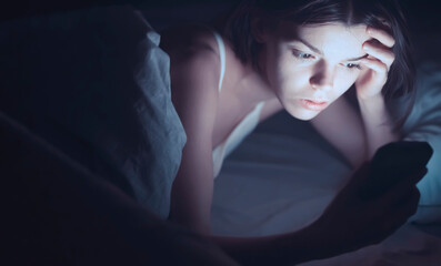 A young girl lies in bed and cannot sleep, reads and chat on social networks on a smartphone. A woman with insomnia is watching a video online on a device.