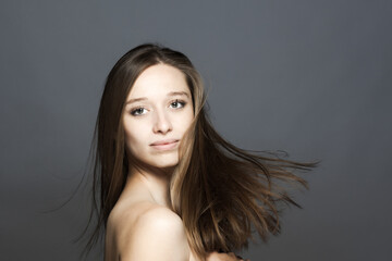brunette girl turning head with flowing hair in the air studio portrait against gray background..