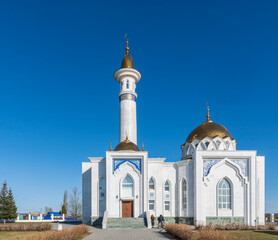 Beautiful Muslim white mosque stands against blue spring sky. There are children at entrance.