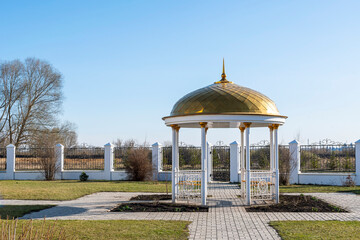 White gazebo with golden dome stands in park on territory of Muslim mosque.