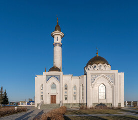 Building of white cathedral Muslim mosque with minaret against blue spring sky.