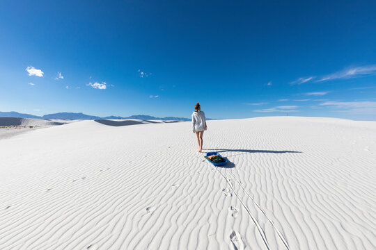 United States, New Mexico, White Sands National Park, Teenage girl pulling sled in desert