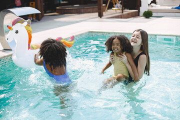 Two african american daughters and their caucasian mother swimming in the pool