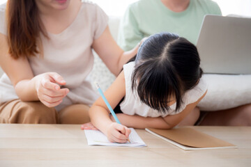 Happy family with mother teaching homework with daughter and father working with laptop on sofa in living room at home, mom explaining schoolwork with kid together, lifestyles and education.