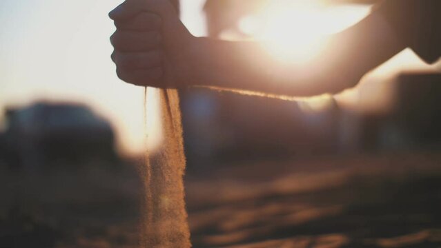 A man pours sand out of his hand in the middle of the desert at the setting sun.