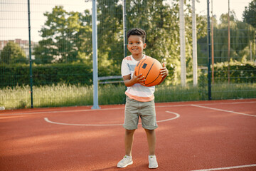 Multiracial boy standing on a basketball court and play with an orange ball