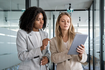 Two businesswoman working together using digital tablet pc and talking about a business project....