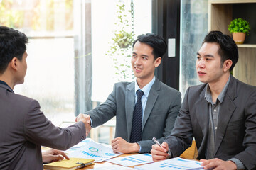 Asian business partners in elegant suits join forces in the real estate business in the office to work together as a team to grow their business.