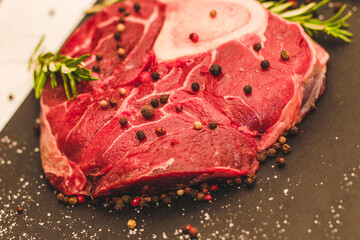 Fresh piece of meat large beef steak on the bone ossobuco with a sprig of rosemary on a black background.