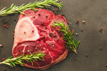 Fresh piece of meat large beef steak on the bone ossobuco with a sprig of rosemary on a black background. - obrazy, fototapety, plakaty
