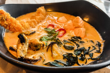 Thai tom yum soup in a plate with seafood, seaweed close-up.