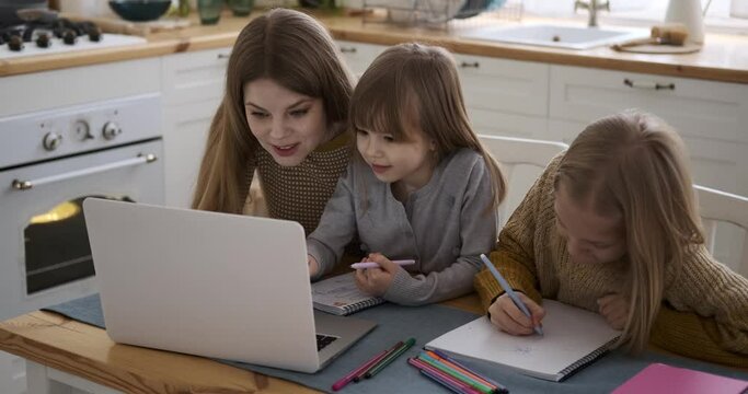 Smiling caucasian young mother showing pictures over laptop to daughters drawing in books on table at home Generative AI